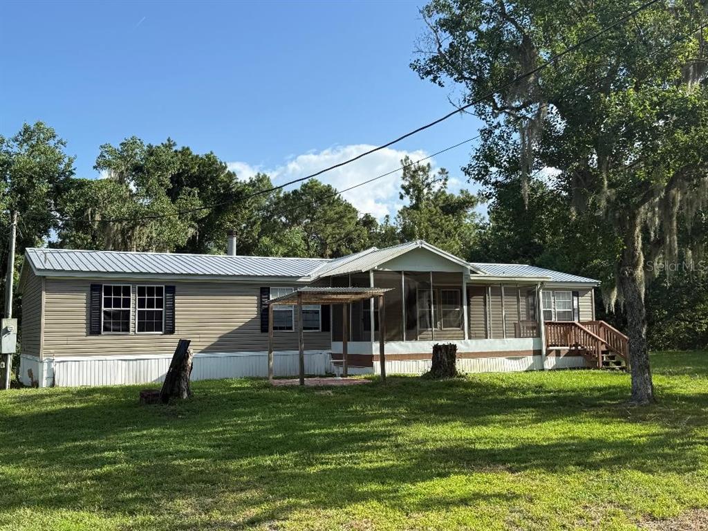 A single-story manufactured home with a metal roof, screened porch, and wooden deck — 129 PATRICIAN PLACE, SATSUMA, FL