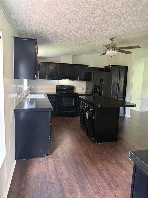 A kitchen features black cabinets, dark countertops, a central island, and wood-look flooring — 129 PATRICIAN PLACE, SATSUMA, FL