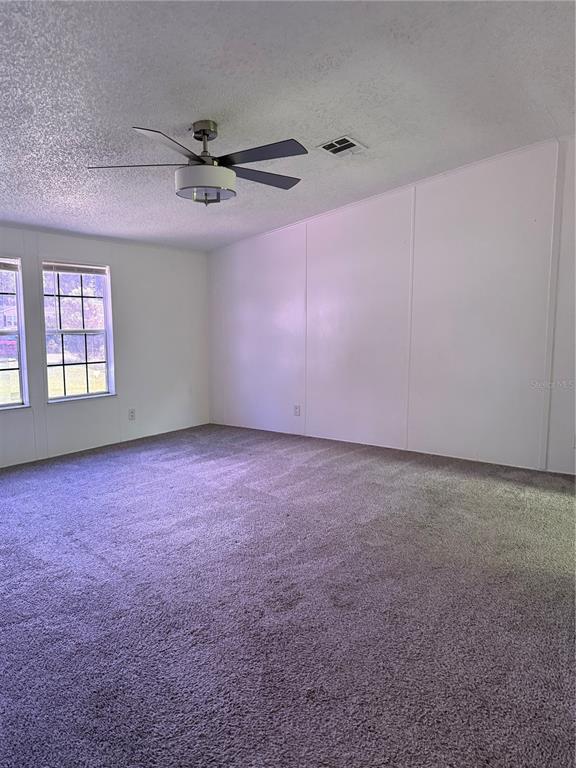 An empty room with gray carpet, white paneled walls, two windows, and a ceiling fan — 129 PATRICIAN PLACE, SATSUMA, FL