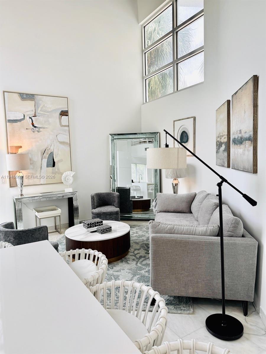 A modern living room features a grey sofa, a round coffee table, and tall windows — 7700 Collins Ave # 5, Miami Beach FL 33141, MIAMI BEACH, FL