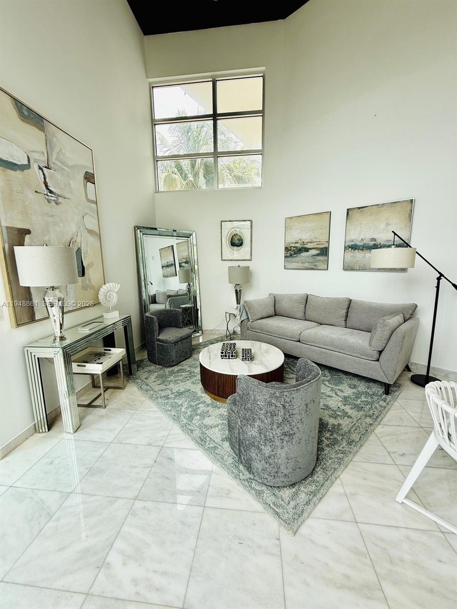 A living room features a gray sofa, two velvet chairs, a coffee table, and tall windows — 7700 Collins Ave # 5, Miami Beach FL 33141, MIAMI BEACH, FL