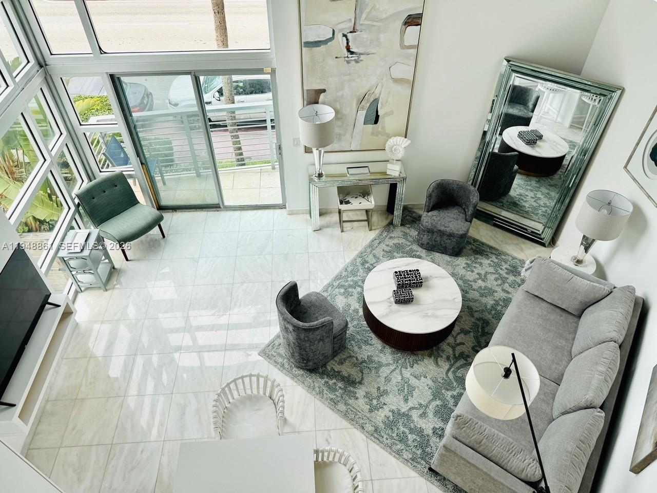 A high-angle view of a modern living room featuring marble floors, floor-to-ceiling windows, and furniture — 7700 Collins Ave # 5, Miami Beach FL 33141, MIAMI BEACH, FL