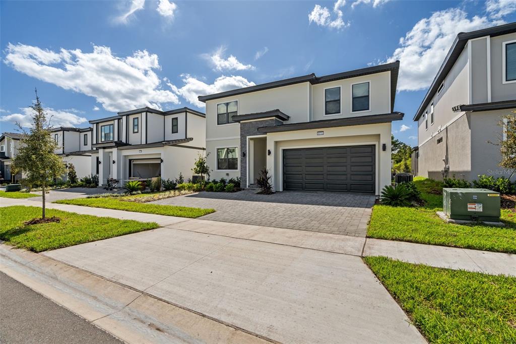 A two-story modern house with a gray garage and a paved driveway under a blue sky — 5773 HIGH SEAS DRIVE, ORLANDO, FL