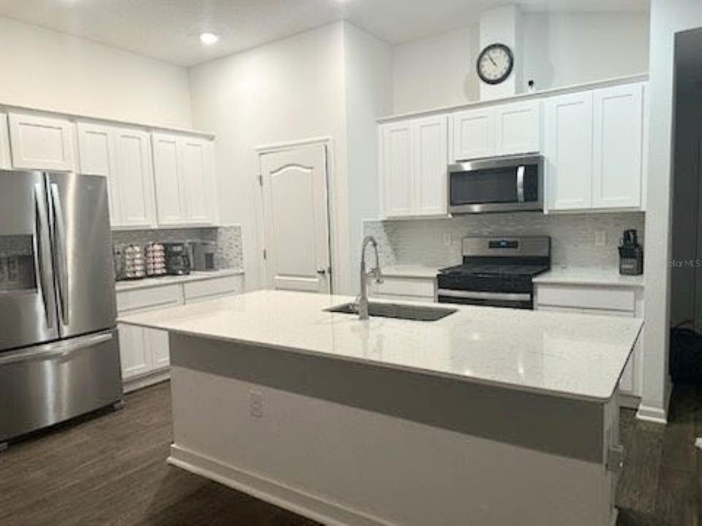 A modern kitchen features white cabinets, stainless steel appliances, and a large central island — 1 CADDY COURT, BUNNELL, FL