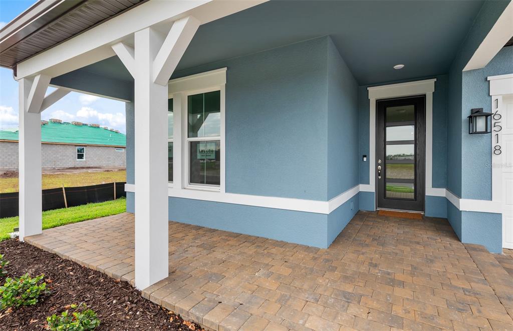 A covered front porch with paver flooring leads to a dark glass-paneled front door — 16518 ENNIS PLACE, BRADENTON, FL