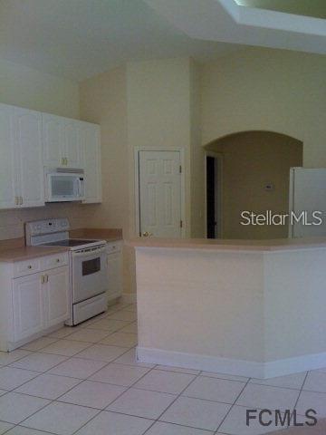 A kitchen features white cabinets, a white stove, and a breakfast bar with tile flooring — 60 PERTHSHIRE LANE, PALM COAST, FL