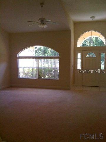 A living room features beige carpeting, a ceiling fan, and an arched window — 60 PERTHSHIRE LANE, PALM COAST, FL