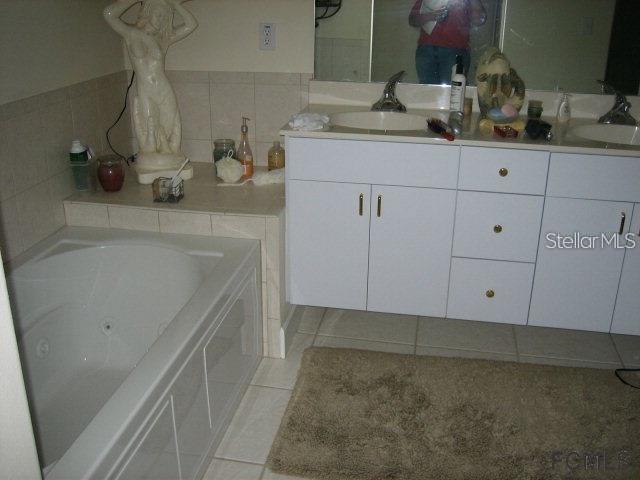 A bathroom features a white vanity with double sinks, a jetted tub, and tiled surfaces — 60 PERTHSHIRE LANE, PALM COAST, FL