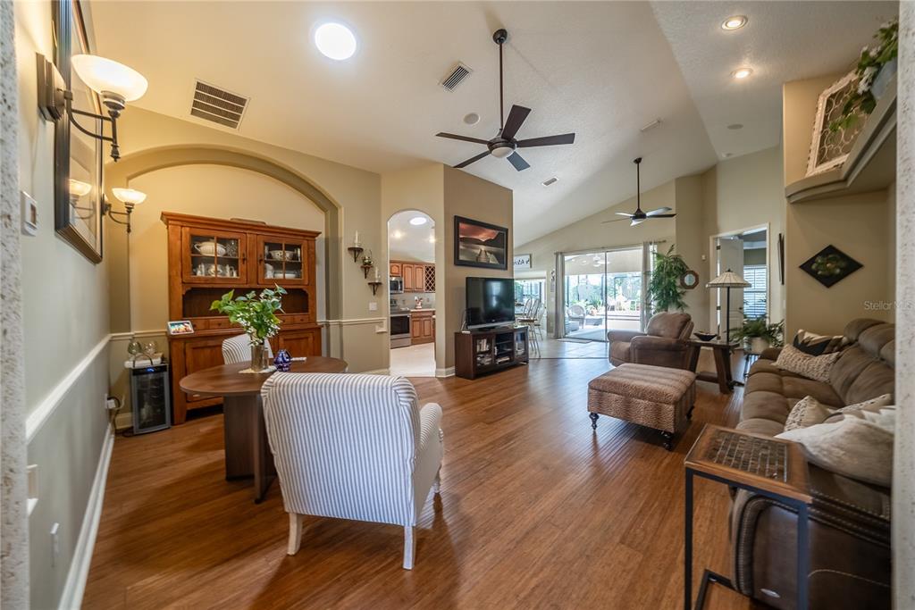 An open-concept living and dining area features wood flooring, vaulted ceilings, and a kitchen view — 710 LAKE DIAMOND AVENUE, OCALA, FL