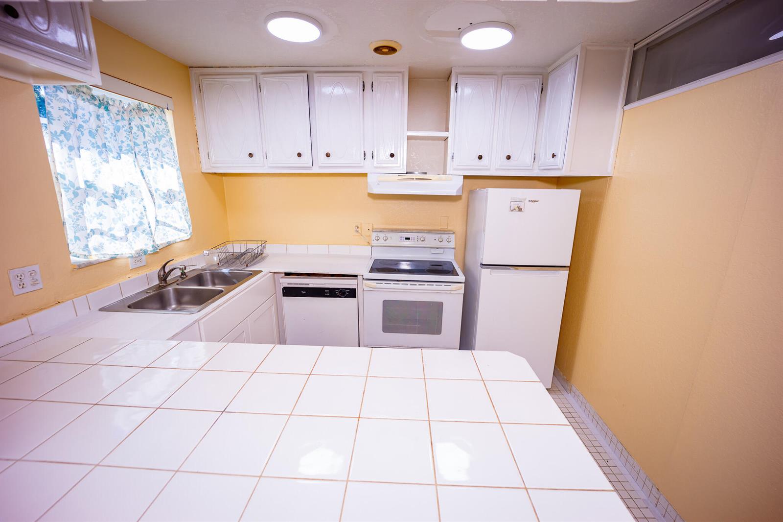 A kitchen with white cabinets, white appliances, tiled countertops, and yellow walls — 3240 Ridge Hill Road # C, Boynton Beach FL 33435, BOYNTON BEACH, FL