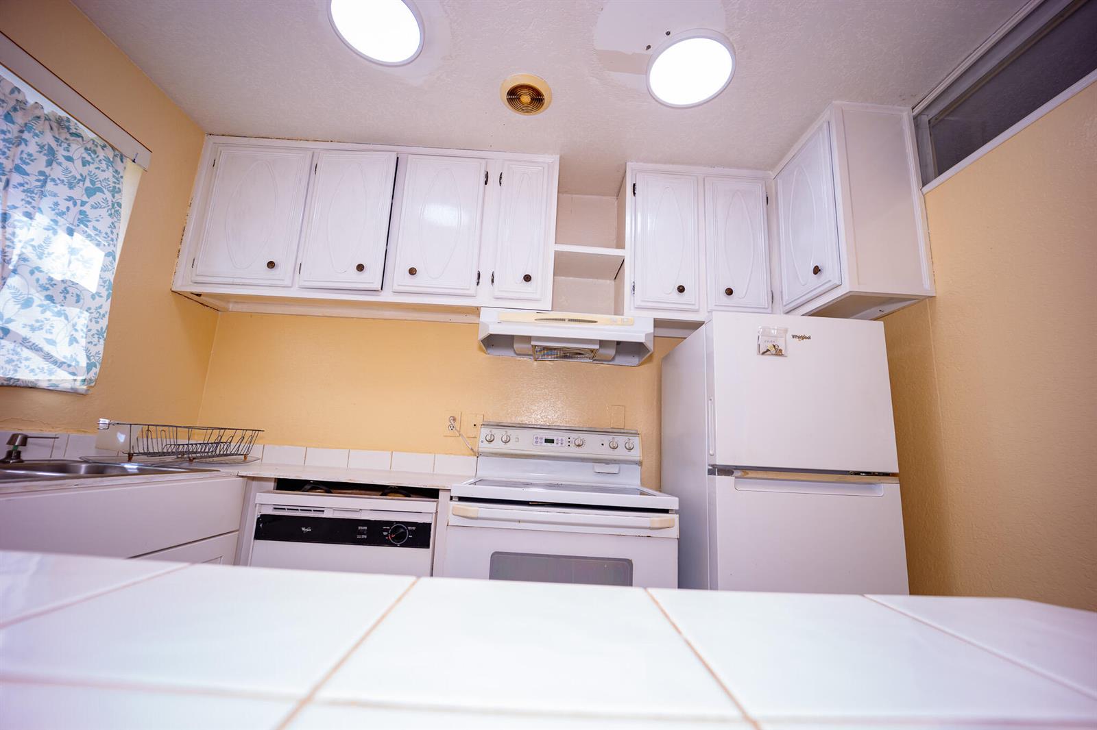 A kitchen features white cabinets, white appliances, yellow walls, and a tiled countertop — 3240 Ridge Hill Road # C, Boynton Beach FL 33435, BOYNTON BEACH, FL