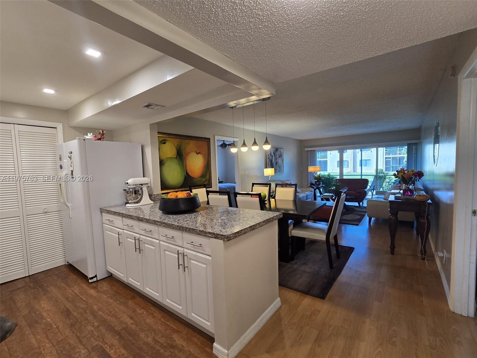 A kitchen island with white cabinets and granite countertops overlooks a dining and living area — 140 Lakeview Dr # 111, Weston FL 33326, WESTON, FL