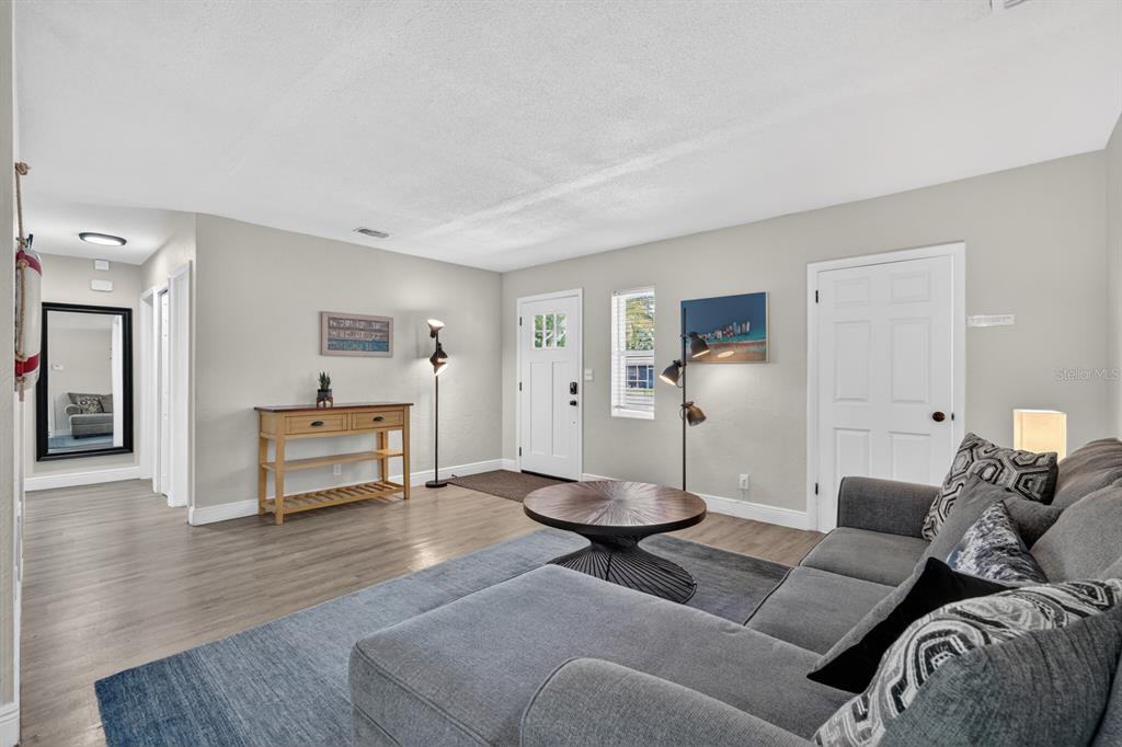 A living room features gray wood-look flooring, a sectional sofa, and a white front door — 1030 ALICE DRIVE, DAYTONA BEACH, FL