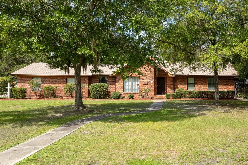 A single-story brick house with a shingled roof sits behind a large lawn and trees — 1619 RAIFORD ROAD, STARKE, FL