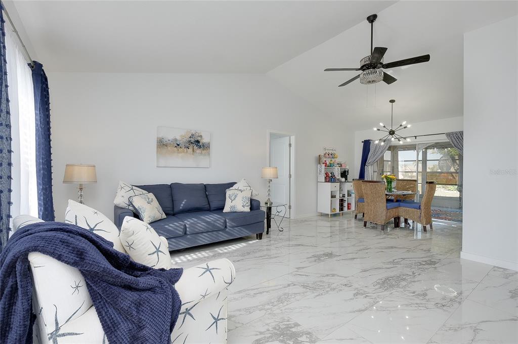 A living room and dining area with white marble floors, blue furniture, and vaulted ceilings — 6433 GRANGER ROAD, PORT CHARLOTTE, FL