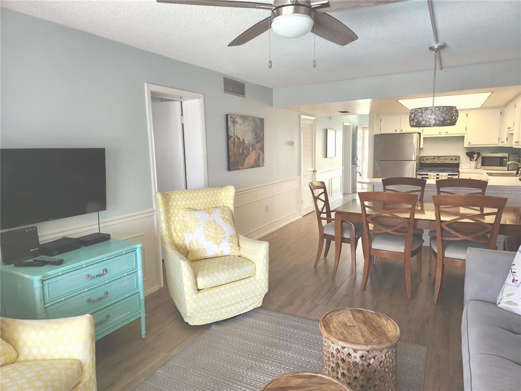 A living and dining area features light blue walls, wood-look flooring, and yellow patterned chairs — 504 FILLMORE AVENUE UNIT B8, CAPE CANAVERAL, FL