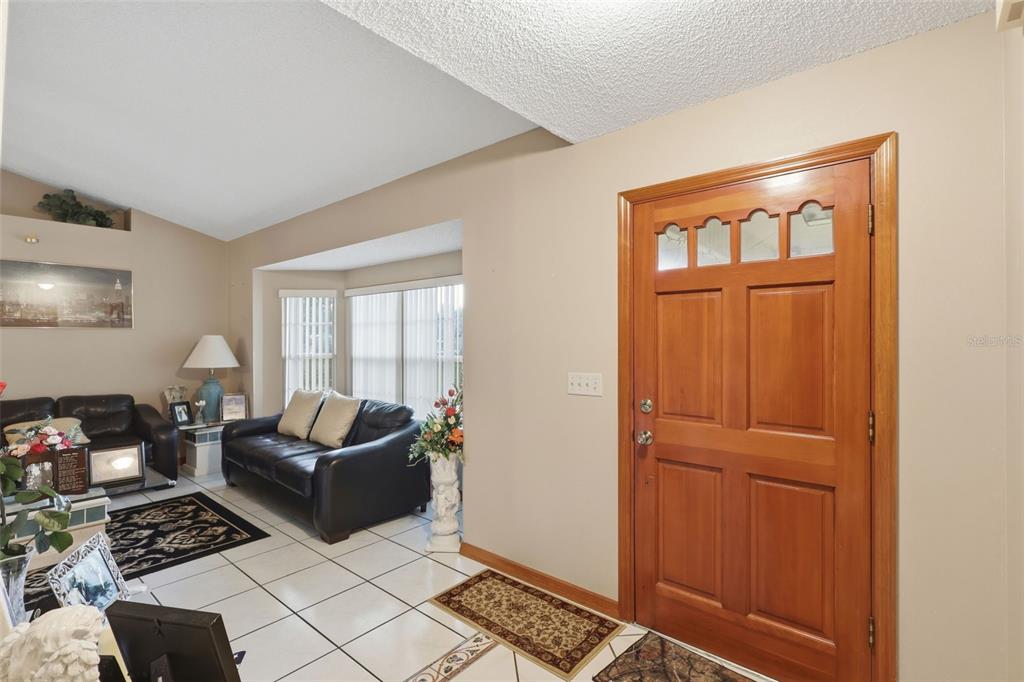 A living room with white tile floors, a wooden front door, and a black leather sofa — 2307 FITZPATRICK TERRACE, DELTONA, FL