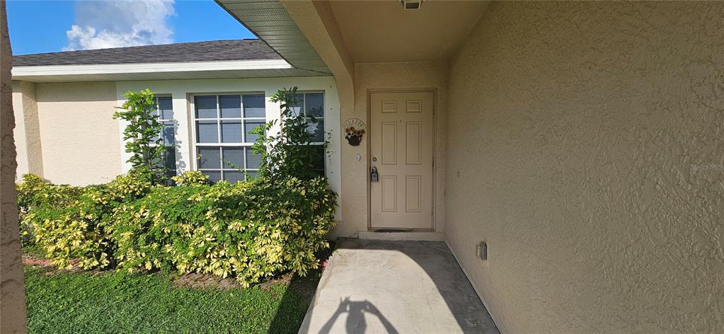 A beige stucco house exterior features a front door, a concrete walkway, and landscaped bushes — 3740 SW SANTA BARBARA PLACE, CAPE CORAL, FL