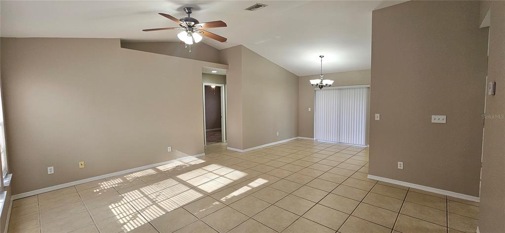 An open-concept living area features vaulted ceilings, tile flooring, a ceiling fan, and sliding doors — 3740 SW SANTA BARBARA PLACE, CAPE CORAL, FL
