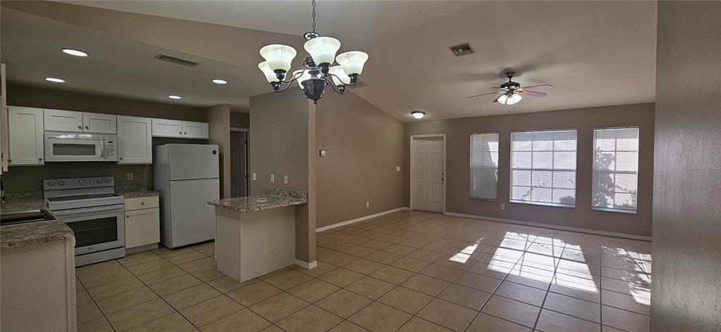 An open-concept kitchen and living area features white cabinetry, tile flooring, and a vaulted ceiling — 3740 SW SANTA BARBARA PLACE, CAPE CORAL, FL
