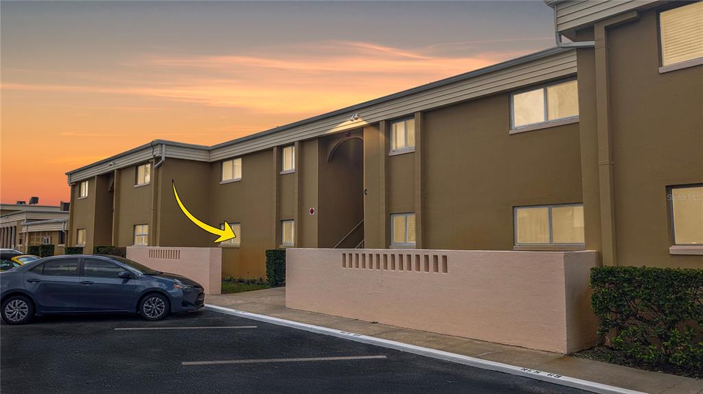 A two-story apartment building exterior features tan stucco walls, a parking lot, and a walkway — 1000 LAKE OF THE WOODS BOULEVARD UNIT C103, FERN PARK, FL