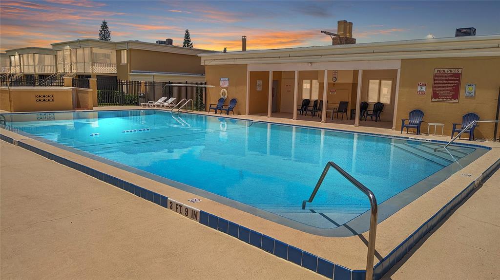 An outdoor swimming pool with a shallow end and surrounding patio area at sunset — 1000 LAKE OF THE WOODS BOULEVARD UNIT C103, FERN PARK, FL
