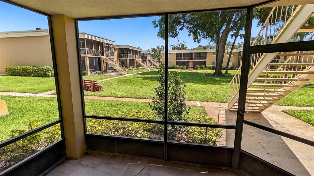 A view from a screened-in porch looking out onto a grassy courtyard and apartment buildings — 1000 LAKE OF THE WOODS BOULEVARD UNIT C103, FERN PARK, FL