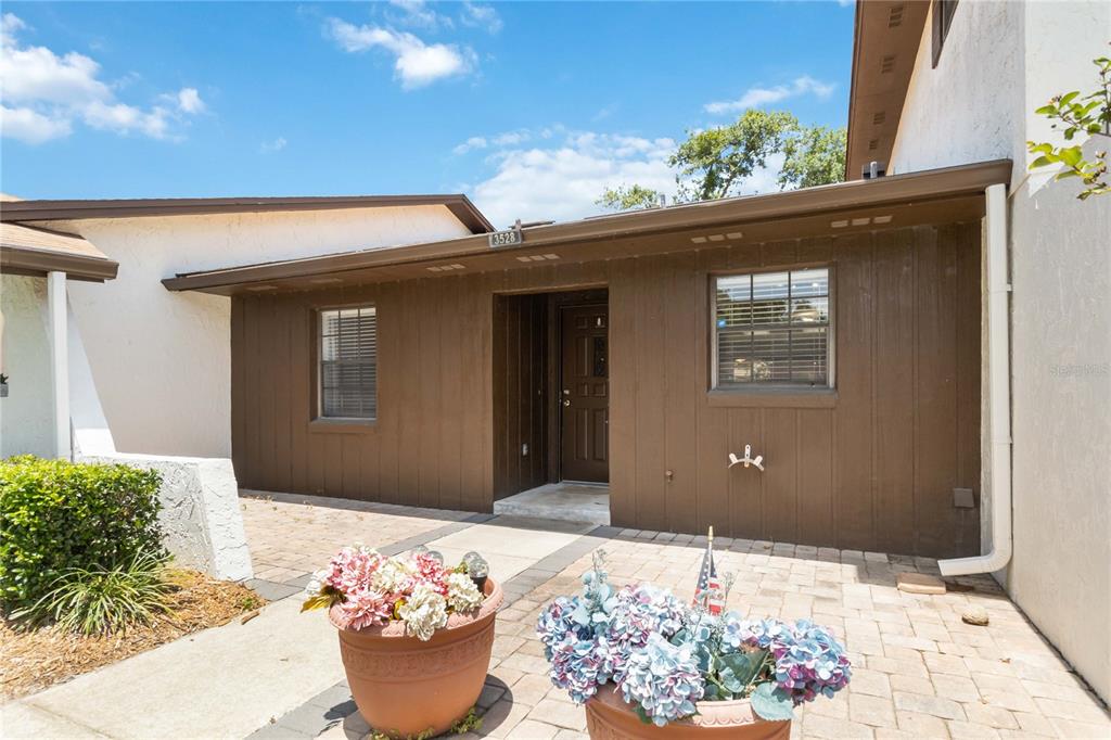 A brown-sided house exterior features a paved patio, two potted plants, and a front door — 3528 BAY CT, ST CLOUD, FL