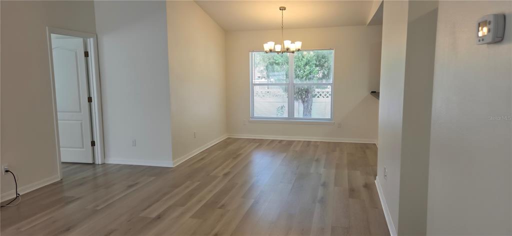 An empty dining room features light wood-look flooring, a chandelier, and a large window — 298 HAMMOCK COURT, DAVENPORT, FL