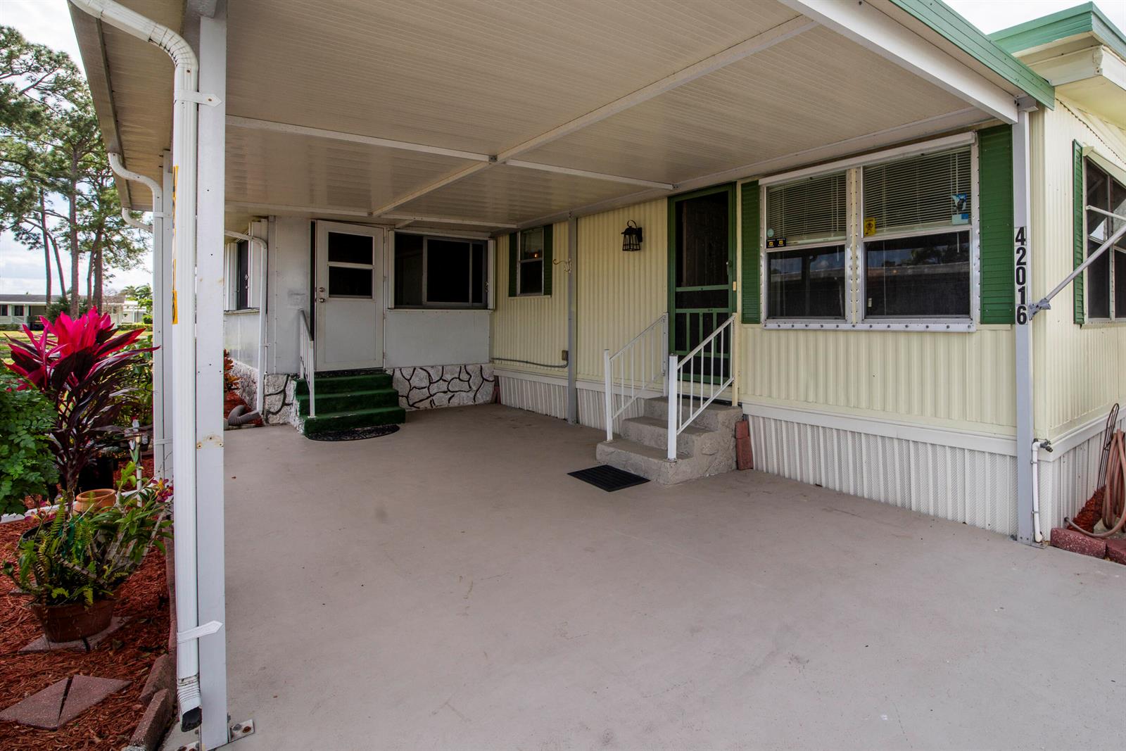 A covered carport area features a concrete floor, two entry doors with stairs, and siding — 42016 Jima Bay, Boynton Beach FL 33436, BOYNTON BEACH, FL