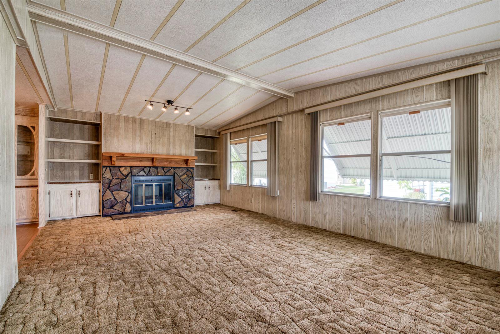 A living room features wood-paneled walls, a stone fireplace, built-in shelving, and brown carpet — 42016 Jima Bay, Boynton Beach FL 33436, BOYNTON BEACH, FL