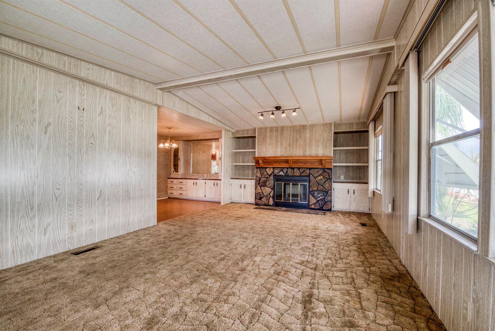 A living room features wood-paneled walls, a stone fireplace, built-in shelving, and brown patterned carpet — 42016 Jima Bay, Boynton Beach FL 33436, BOYNTON BEACH, FL