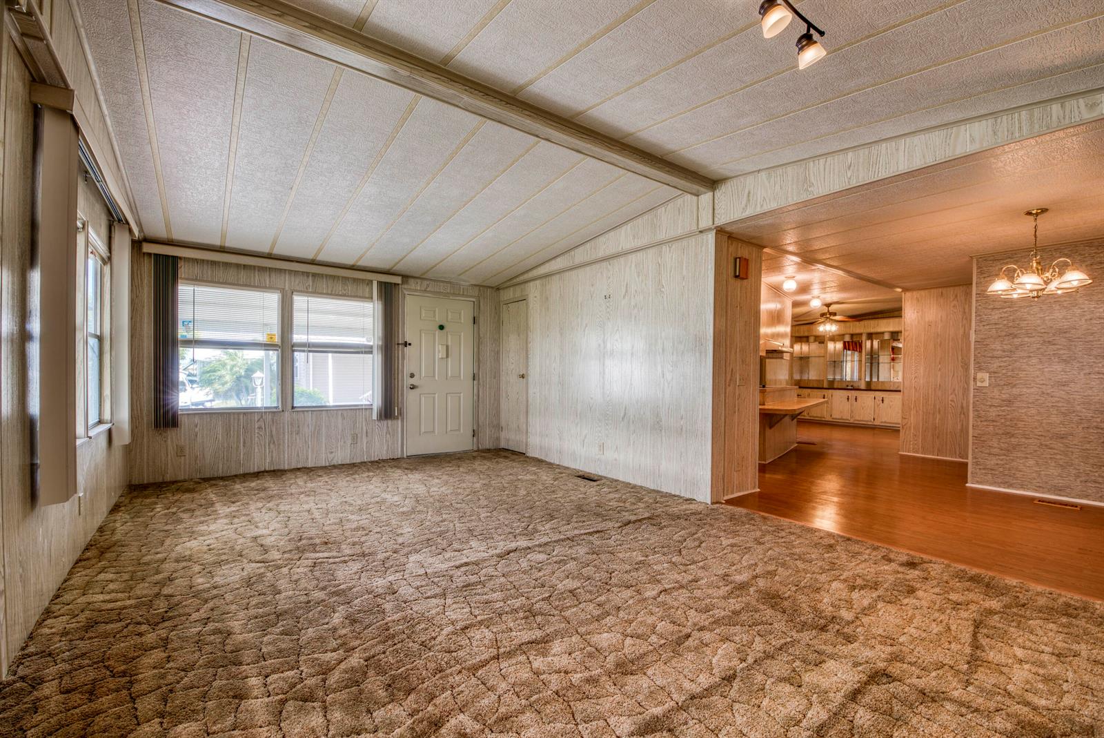 A living room with brown carpet and wood-paneled walls leads into a dining area — 42016 Jima Bay, Boynton Beach FL 33436, BOYNTON BEACH, FL
