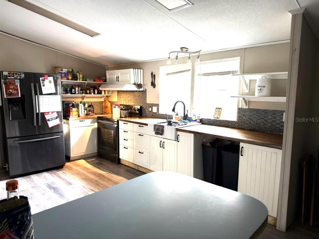 A kitchen features white cabinets, a farmhouse sink, dark countertops, and a black refrigerator — 4126 W BELLA VISTA STREET, LAKELAND, FL