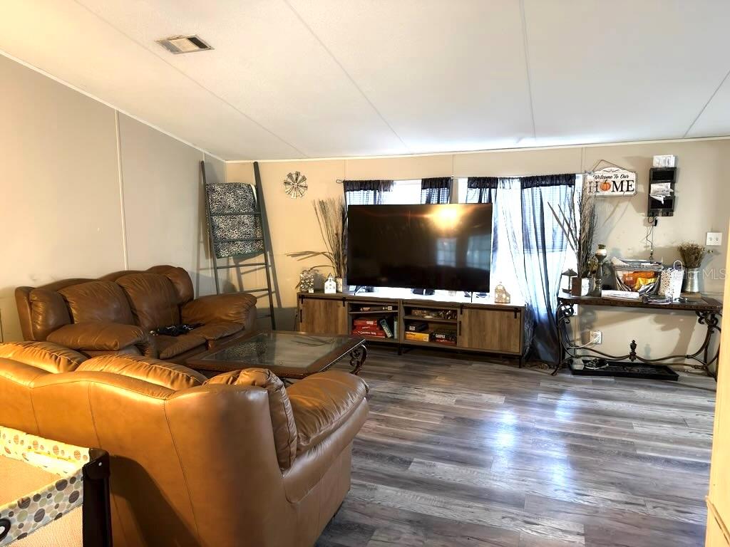 A living room features brown leather sofas, a large television on a console, and wood-look flooring — 4126 W BELLA VISTA STREET, LAKELAND, FL