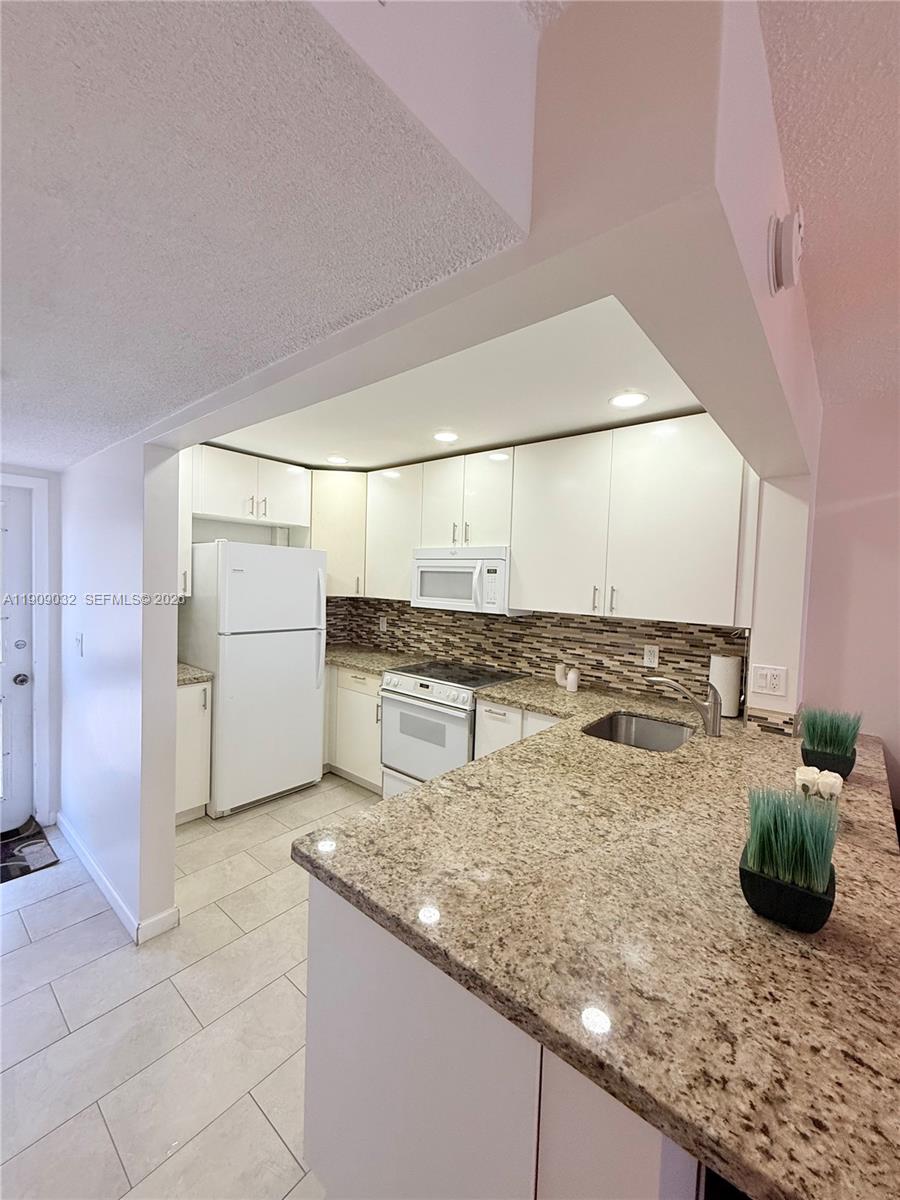 A kitchen features white cabinets, granite countertops, a tiled backsplash, and white appliances — 2081 S Ocean Dr # 308, Hallandale Beach FL 33009, HALLANDALE BEACH, FL
