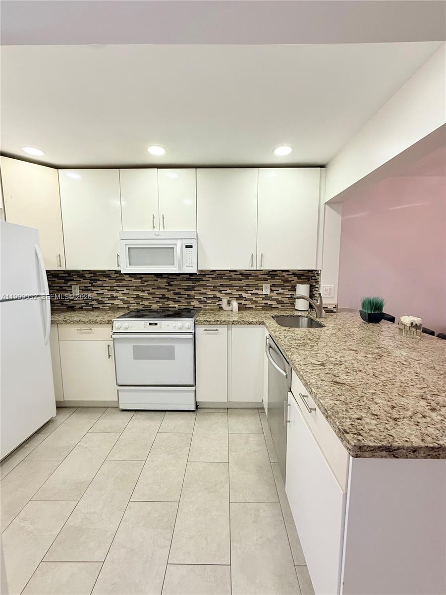 A kitchen features white cabinets, granite countertops, a tiled backsplash, and stainless steel appliances — 2081 S Ocean Dr # 308, Hallandale Beach FL 33009, HALLANDALE BEACH, FL