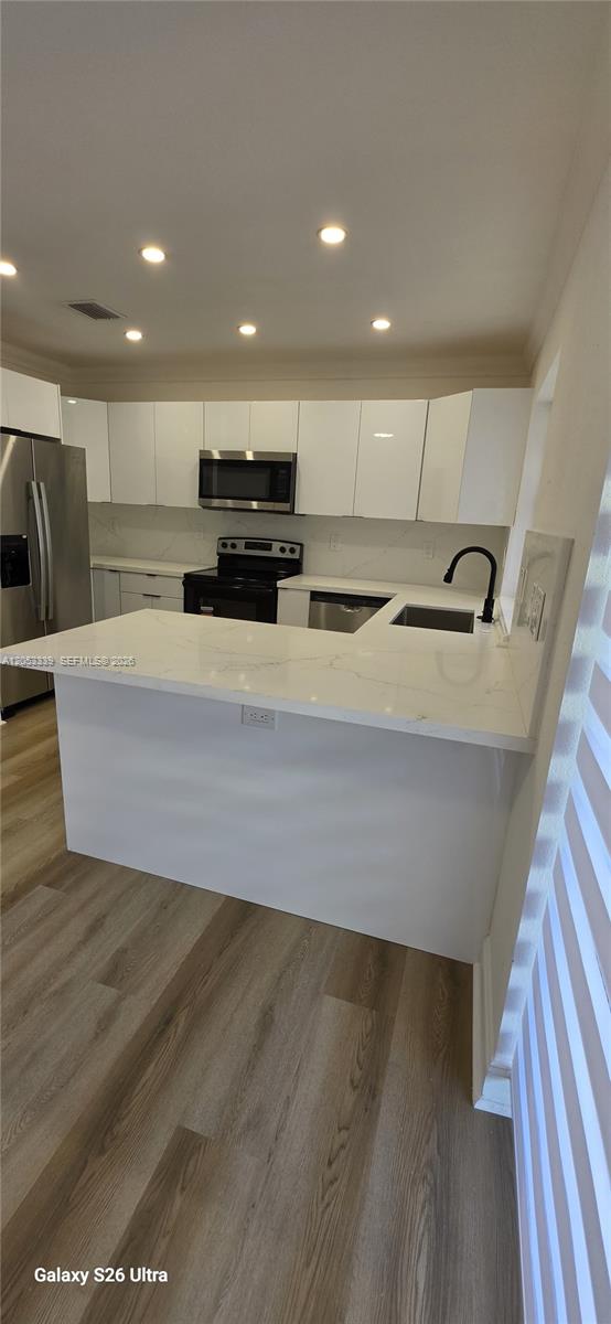 A modern kitchen features white cabinets, a quartz peninsula, stainless steel appliances, and wood-look flooring — 19225 Franjo Rd, Cutler Bay FL 33157, CUTLER BAY, FL