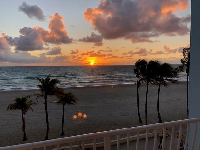 A balcony view overlooking a sandy beach and ocean at sunset with palm trees — 300 E Oregon Street E # 303, Hollywood FL 33019, HOLLYWOOD, FL