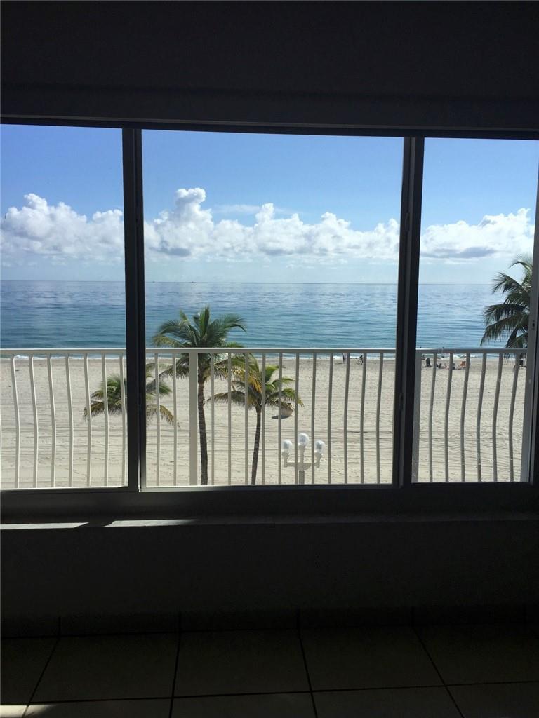 A view of the beach and ocean through a large window with a white railing — 300 E Oregon Street E # 303, Hollywood FL 33019, HOLLYWOOD, FL