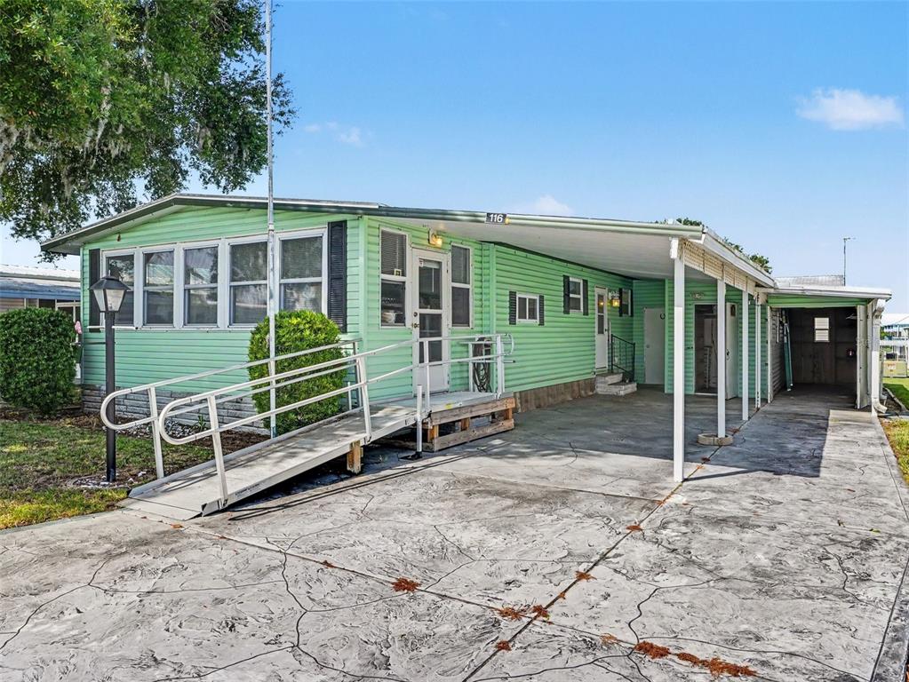 A light green mobile home features a concrete driveway, a carport, and a wheelchair ramp — 116 PINE TERRACE, HAINES CITY, FL