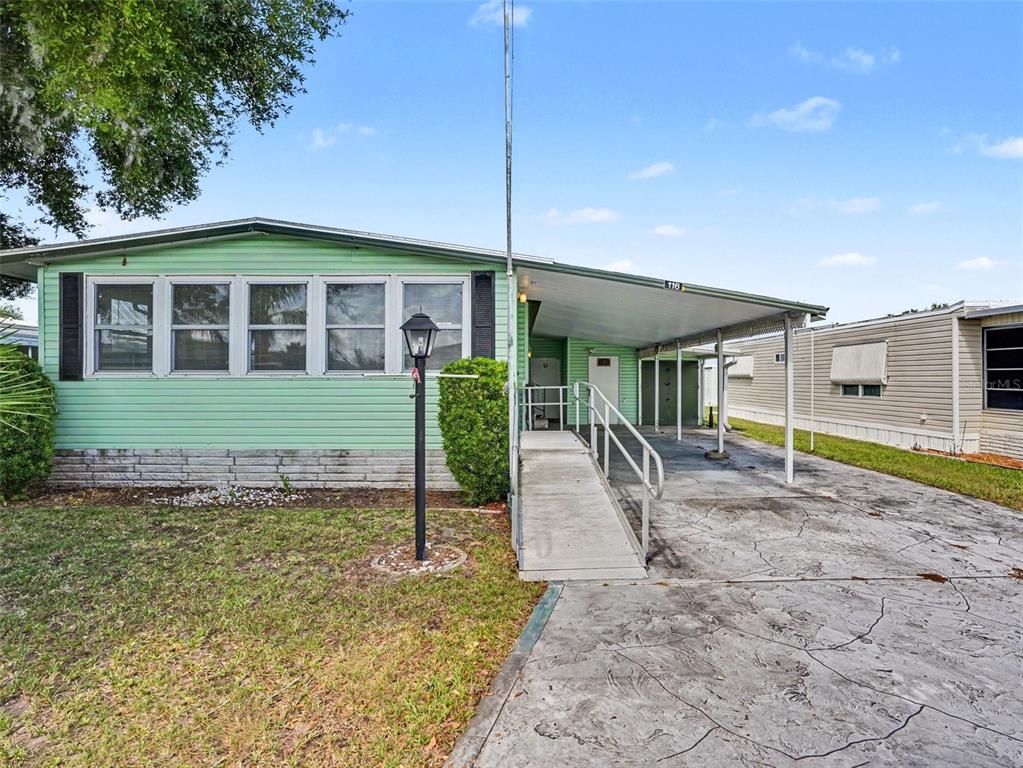 A light green mobile home features a concrete driveway, a carport, and an accessibility ramp — 116 PINE TERRACE, HAINES CITY, FL