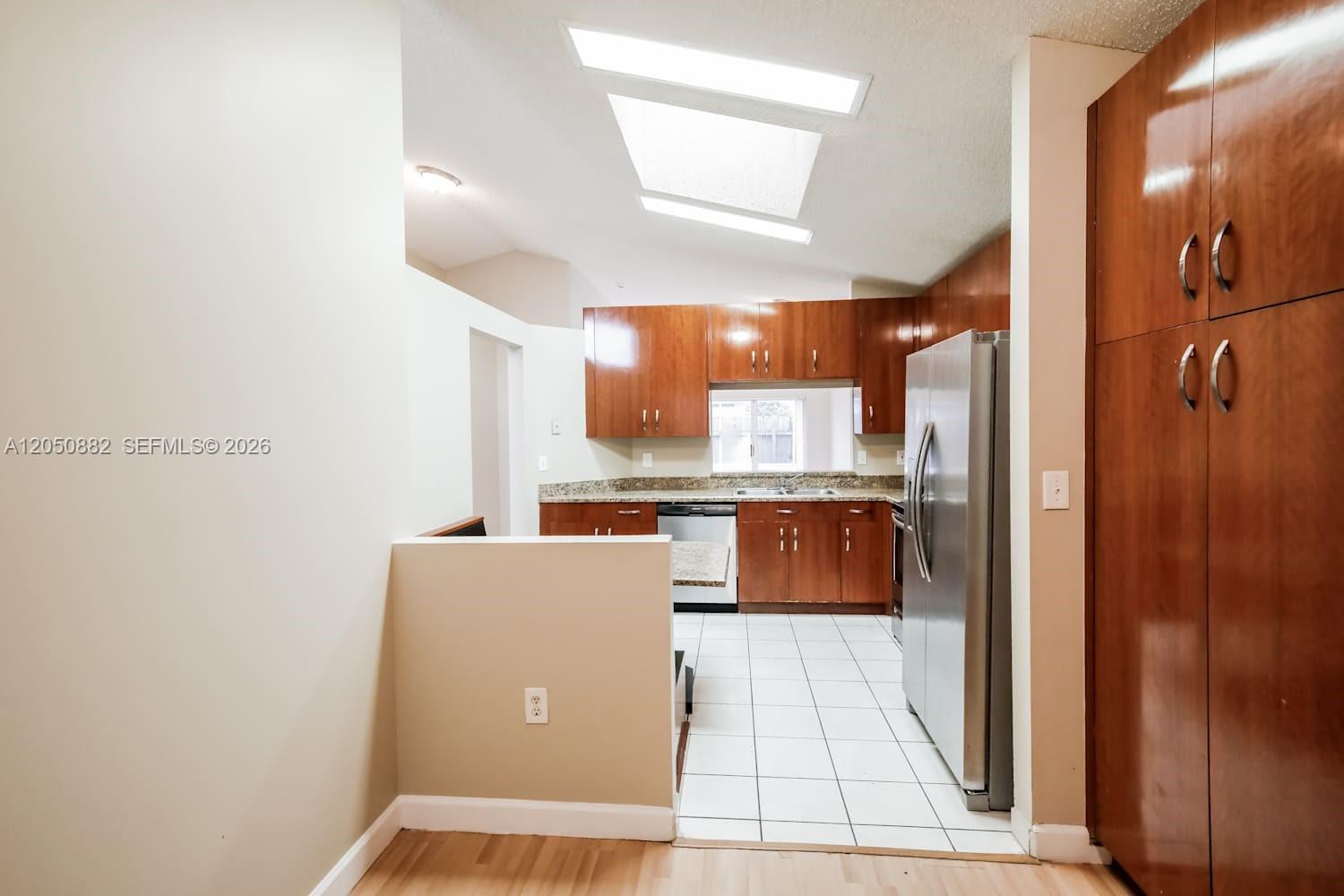 A kitchen features wood cabinets, stainless steel appliances, tile flooring, and a large skylight — CUTLER BAY, FL