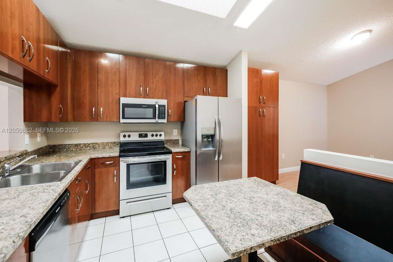 A kitchen features wood cabinets, stainless steel appliances, granite countertops, and a built-in dining booth — CUTLER BAY, FL