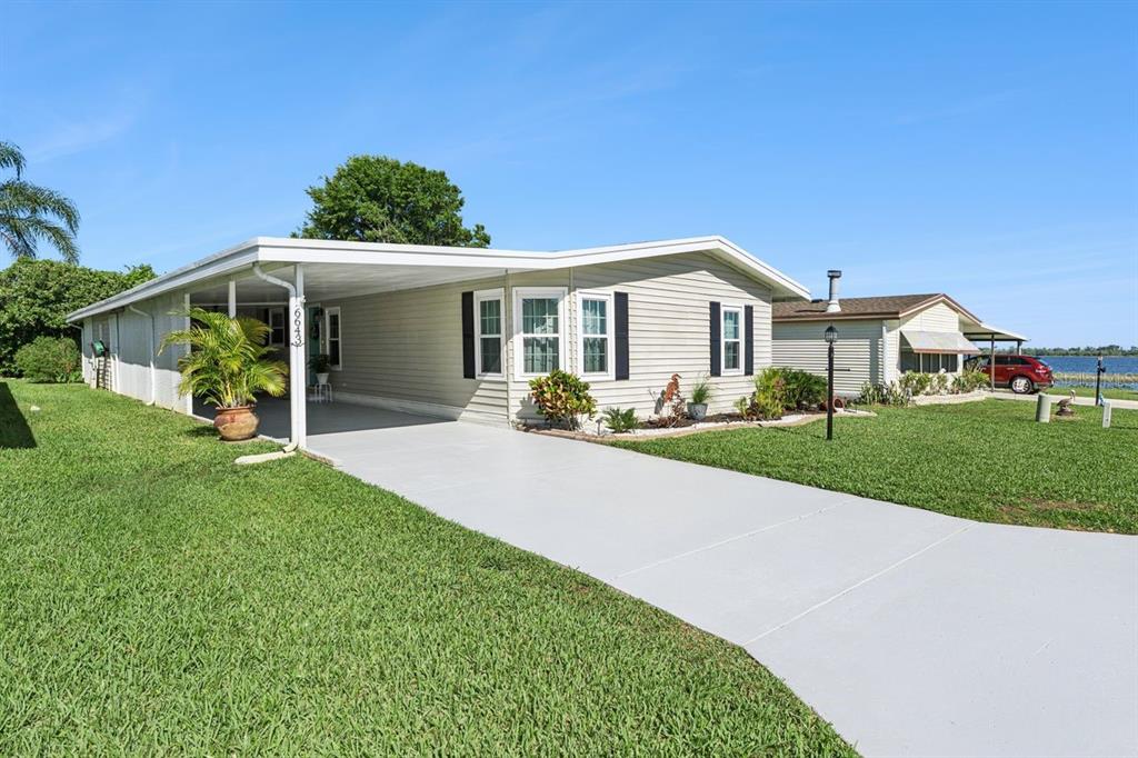 A light-colored mobile home with a carport and a concrete driveway sits on a lawn — 6643 WESTCHESTER DRIVE NE, WINTER HAVEN, FL