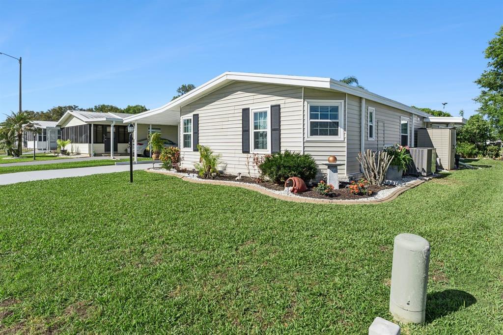 A light-colored mobile home with a carport and landscaped front yard under a blue sky — 6643 WESTCHESTER DRIVE NE, WINTER HAVEN, FL
