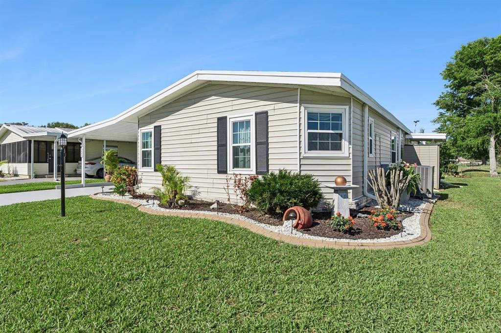 A light-colored mobile home with a carport, black shutters, and landscaped flower beds — 6643 WESTCHESTER DRIVE NE, WINTER HAVEN, FL