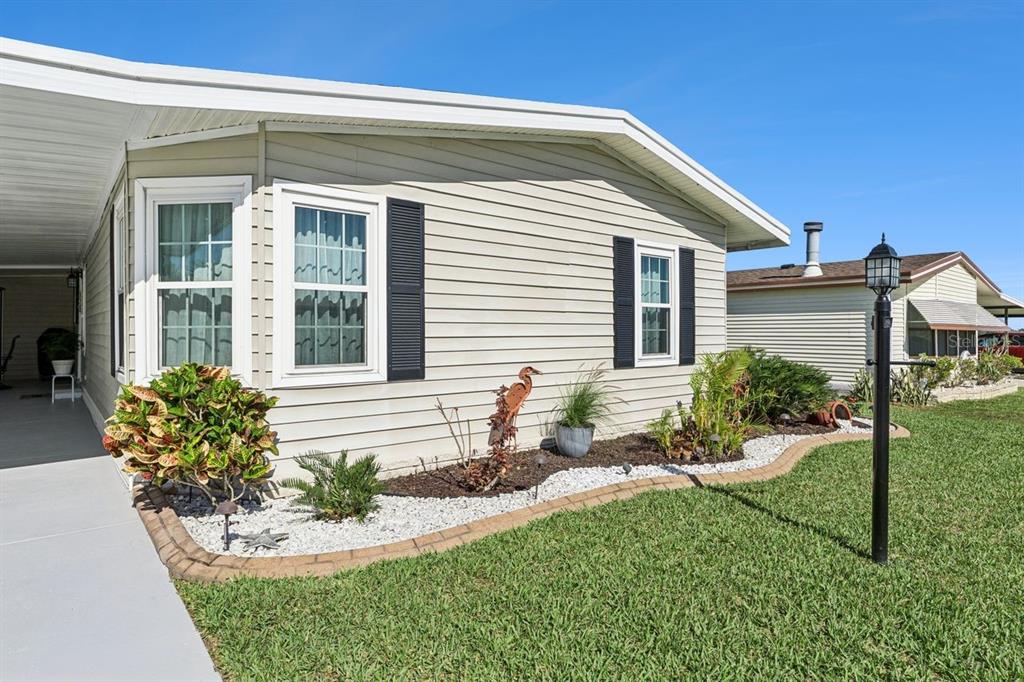The exterior of a light-colored mobile home features a landscaped garden bed and a carport — 6643 WESTCHESTER DRIVE NE, WINTER HAVEN, FL