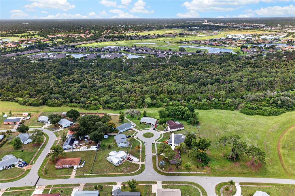 An aerial view shows a suburban neighborhood with houses, a cul-de-sac, and surrounding wooded areas — 6789 MIRO COURT, NORTH PORT, FL