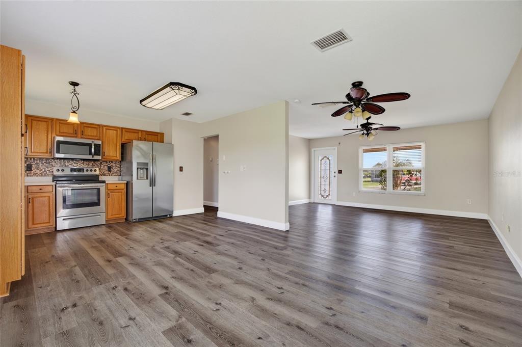 An open-concept kitchen and living area featuring wood-look flooring, light-colored walls, and stainless steel appliances — 6789 MIRO COURT, NORTH PORT, FL